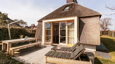 Tuin van een vakantiehuis met rieten dak op vakantiepark Dutchen Park Duynvallei
