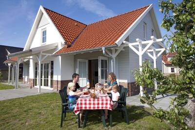 Gezin eet aan een tafel in de tuin van een vakantiehuis op Roompot Résidence Klein Vink