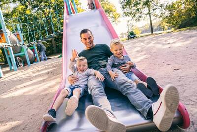 Vader met 2 kinderen op een glijbaan in een speeltuin op Roompot Vakantiepark Weerterbergen
