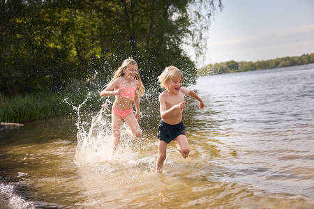 Kinderen rennen door het water van het recreatiemeer (Victoriameer) op Lake Resort Beekse Bergen