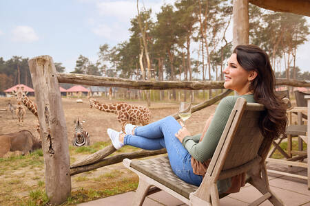 Vrouw kijkt  vanaf het terras van een lodge over de savanne op Safari Resort Beekse Bergen