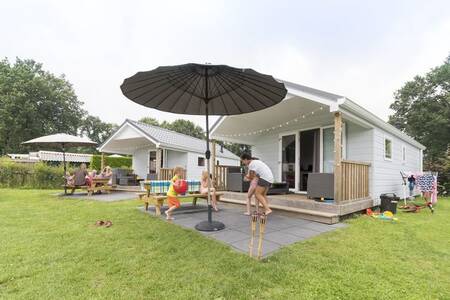 Gezin in de tuin van een Lodge op vakantiepark Camping de Noetselerberg