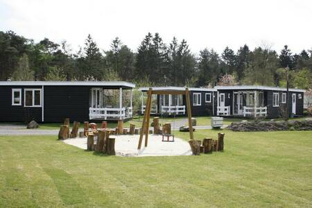 Chalets op een veldje met een speeltuin op vakantiepark Camping de Norgerberg