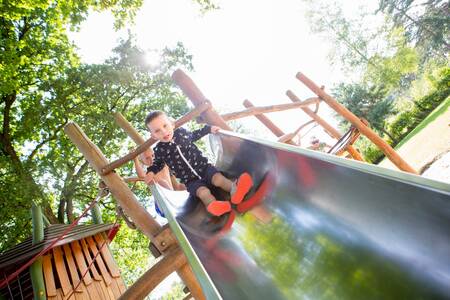 Kind op de glijbaan in een speeltuin op vakantiepark Camping de Norgerberg