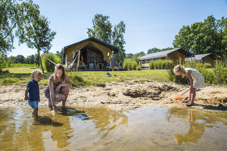 Kinderen spelen in het water van het meertje bij de safaritenten op Camping Vreehorst