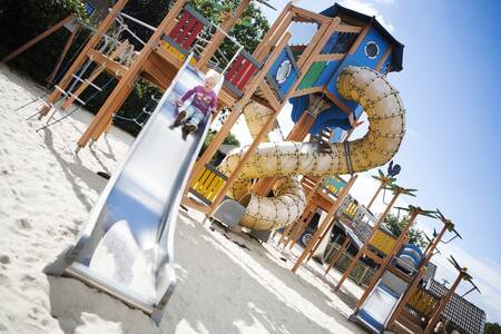 Kindje glijdt van de glijbaan in een speeltuin op vakantiepark De Boshoek