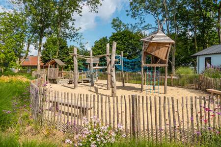 Een omheinde speeltuin met houten speeltoestellen op vakantiepark EuroParcs Aan de Maas