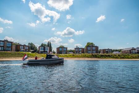 Sloep vaart langs het strand en vakantiehuizen op vakantiepark EuroParcs Aan de Maas