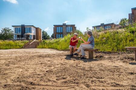 Een paar zit op een bankje op het strand van vakantiepark EuroParcs Aan de Maas