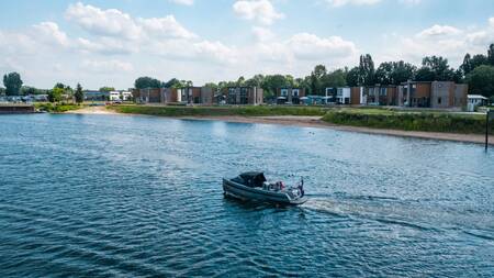 Een sloep vaart voor vakantiehuizen aan het water op vakantiepark EuroParcs Aan de Maas