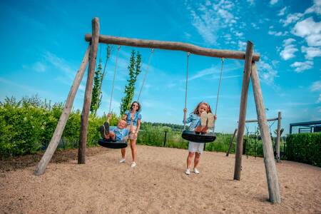 Kinderen op de schommel in een speeltuin op vakantiepark EuroParcs Bad Hulckesteijn