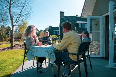 Gezin aan een tafel in de tuin van een vakantiehuis op vakantiepark Europarcs de Achterhoek