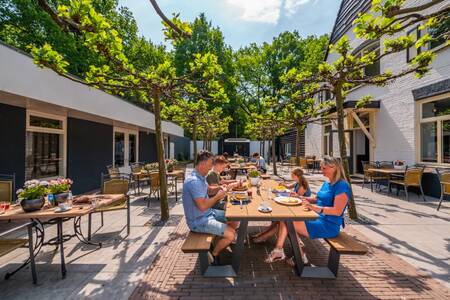 Gezin eet op het terras van het restaurant op vakantiepark EuroParcs De Hooge Veluwe