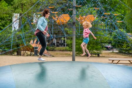 Moeder en kind springen op de airtrampoline in een speeltuin op vakantiepark EuroParcs de Zanding