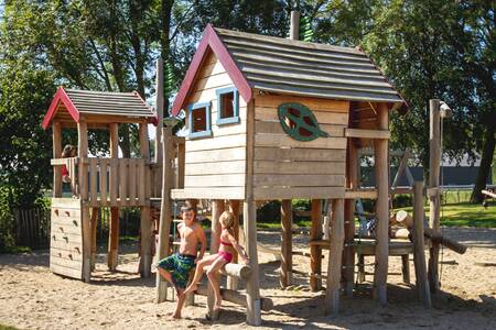 Twee kinderen bij houten speeltoestellen in de speeltuin van vakantiepark EuroParcs Gulperberg