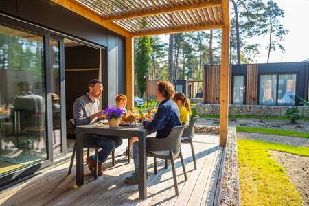 Gezin eet op de veranda van een chalet op vakantiepark EuroParcs Hoge Kempen