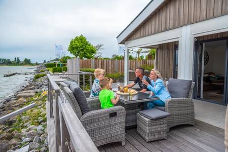 Gezin eet op de veranda van een chalet aan het water op vakantiepark EuroParcs Markermeer