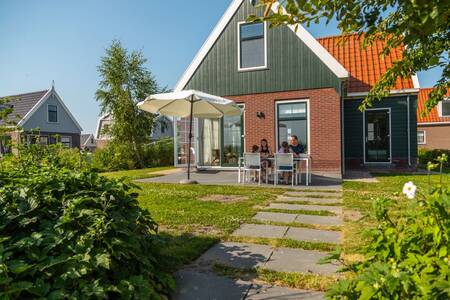 Gezin aan tafel in de tuin van een vakantiehuis op vakantiepark EuroParcs Poort van Amsterdam