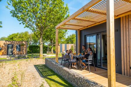 Gezin eet op de veranda van een chalet op vakantiepark EuroParcs Poort van Maastricht