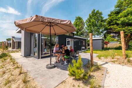 Gezin zit aan tafel in de tuin van een vakantiehuis op vakantiepark EuroParcs Poort van Zeeland