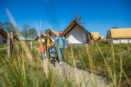 Gezin wandelt tussen glampingtenten op vakantiepark EuroParcs Zuiderzee