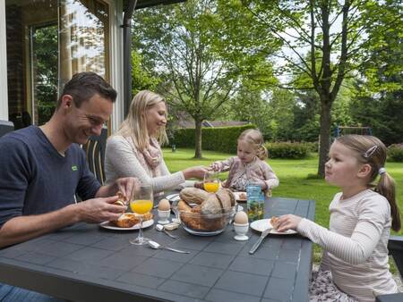 Gezin ontbijt in de tuin van een vakantiehuis op vakantiepark Landal Aelderholt