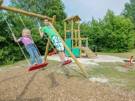 Kinderen spelen op de schommel in een speeltuin op vakantiepark Landal De Bloemert