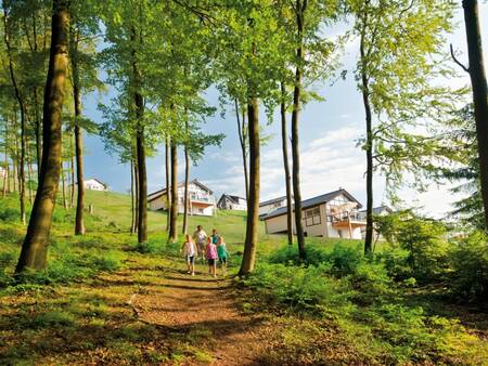 Gezin wandelt tussen bomen met op de achtergrond vakantiehuizen van Landal Winterberg