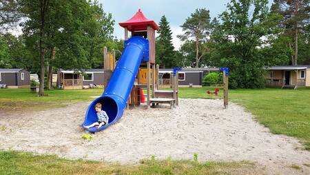 Kind op de glijbaan in een speeltuin tussen chalets op vakantiepark Molecaten Park De Koerberg
