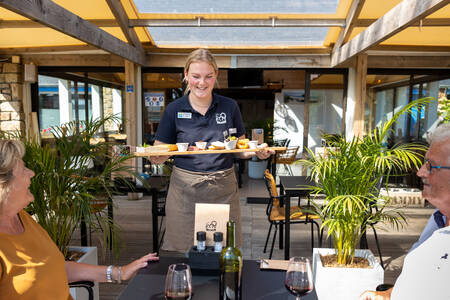 Ober bezorgd hapjes bij een stel op het terras van het restaurant op vakantiepark RCN Port l’Epine