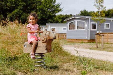 Meisje op een kipwip bij chalets op vakantiepark RCN Toppershoedje