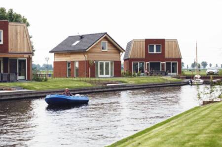 Een sloep vaart voor vakantiehuizen aan het water op vakantiepark Recreatiepark Tusken de Marren