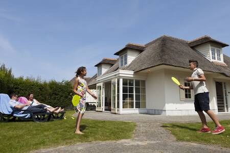 Gezin in de tuin van een vakantiehuis met rieten dak op Roompot Buitenhof Domburg