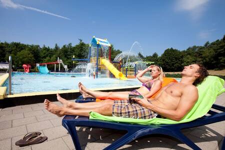 Mensen op ligstoelen bij het buitenbad van vakantiepark Roompot Buitenplaats De Hildenberg