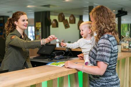 Vrouw met kind neemt sleutel in ontvangst bij de receptie van Roompot Bungalowpark Hoenderloo