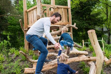 Vader met kinderen in een houten speeltuin op vakantiepark Roompot Bungalowpark Hoenderloo