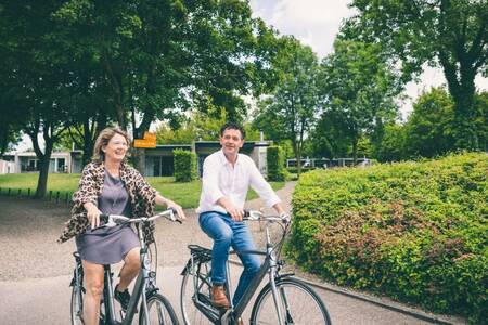 Mensen fietsen tussen vakantiehuizen op vakantiepark Roompot Bungalowpark Schin op Geul
