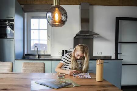 Meisje aan de tafel in de keuken van een vakantiehuis op vakantiepark Roompot De Heihorsten