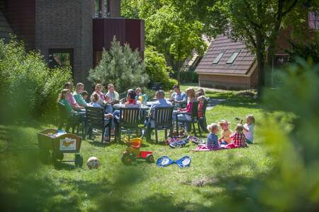 Gezin zit in de tuin van een vakantiehuis op vakantiepark Roompot De Katjeskelder