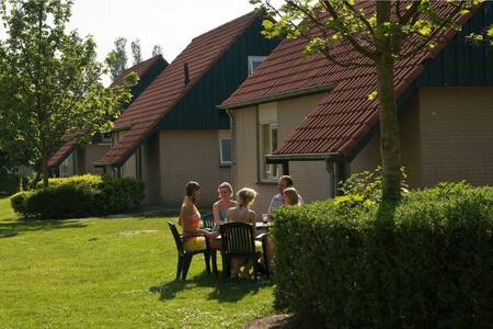 Mensen zitten in de tuin van een vakantiehuis op vakantiepark Roompot Kustpark Klein Poelland