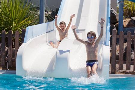 2 kinderen glijden van een dubbele glijbaan in het buitenbad van vakantiepark Roompot Le Littoral