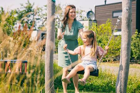 Moeder en dochter op de schommel in de speeltuin op vakantiepark Roompot Park Zeedijk