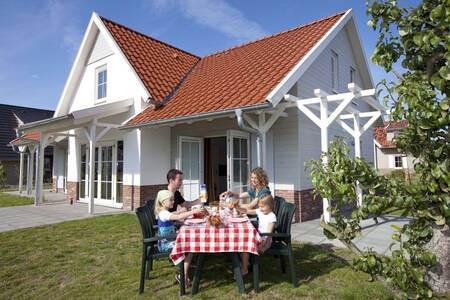 Gezin eet aan een tafel in de tuin van een vakantiehuis op Roompot Résidence Klein Vink