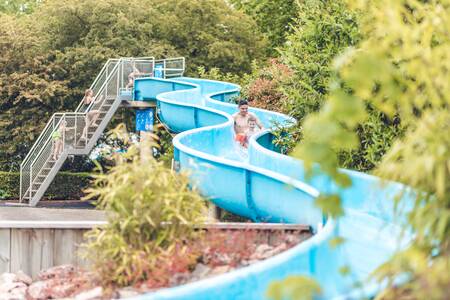 Vader met kind glijdt van de glijbaan in het buitenbad van Veluwepark de Bosgraaf